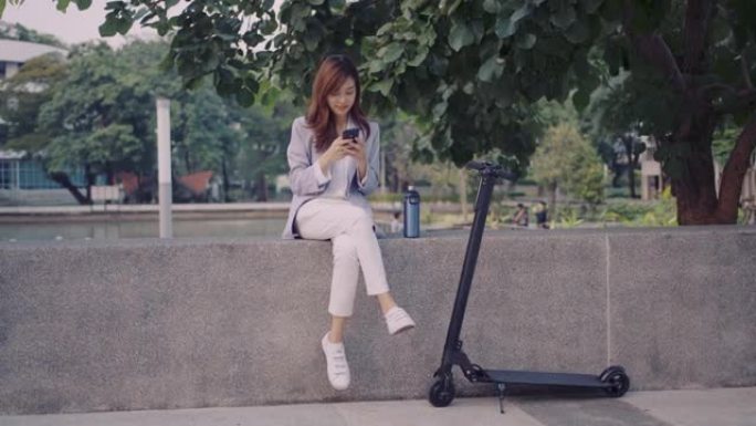 年轻女子坐在公园里，骑着电动摩托车玩手机