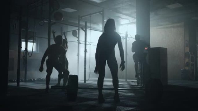 在健身房硬举，苗条的女运动员在黑暗的健身大厅举杠铃的剪影
