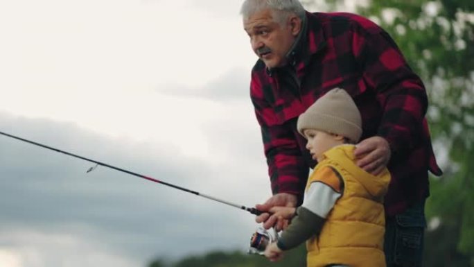 细心的祖父正在教他的孙子在湖里钓鱼，家人在大自然中休息