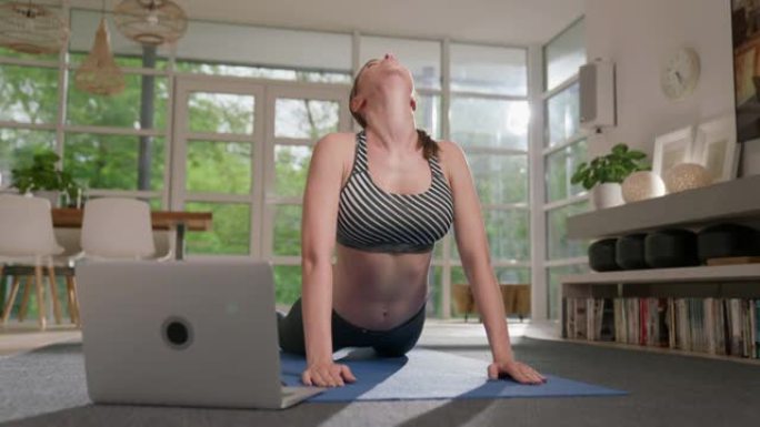 女运动员用笔记本电脑做瑜伽。朝上狗姿势放松的家庭锻炼