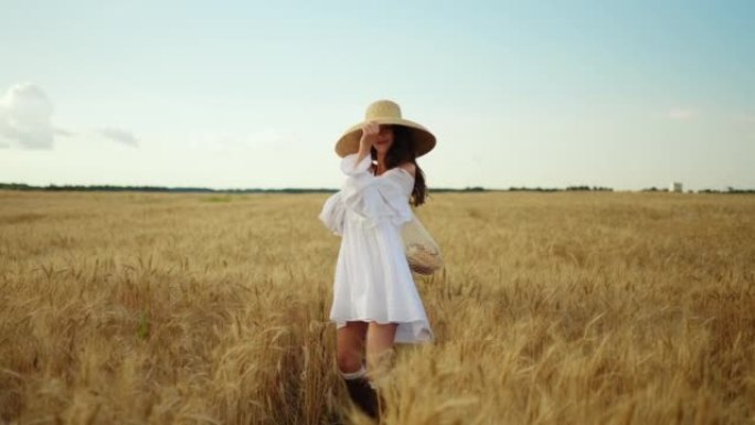 夏日无忧无虑的漂亮女人走在成熟的麦田上，穿着白色连衣裙的女士微笑着