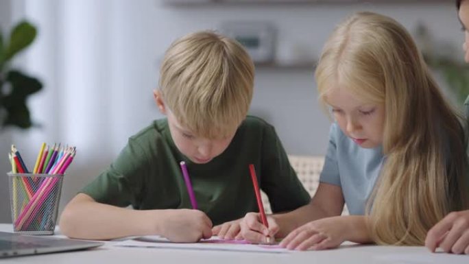 两个孩子坐在桌子旁画画，妈妈帮忙。一个男孩和一个女孩在桌子上画画