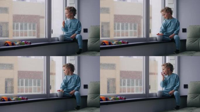 舒适的家庭氛围在冬季周末，可爱的小男孩坐在公寓的窗台上，看着雪花
