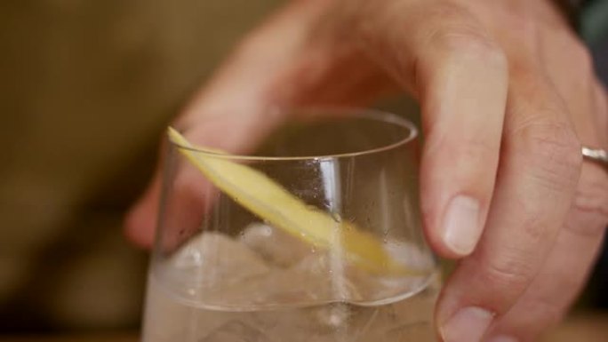 一个男人转动装满苏打水和柠檬苦味的玻璃杯的细节镜头