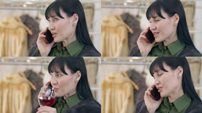 coquette年轻女子在智能手机上聊天的特写镜头，她喝着玻璃杯里的红酒。在时装店或家里，轻浮的高加