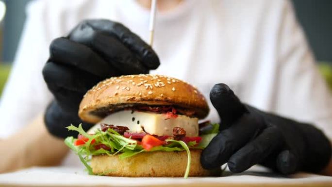 厨师戴着黑手套，用晒干的西红柿和豆腐烹饪素食汉堡。