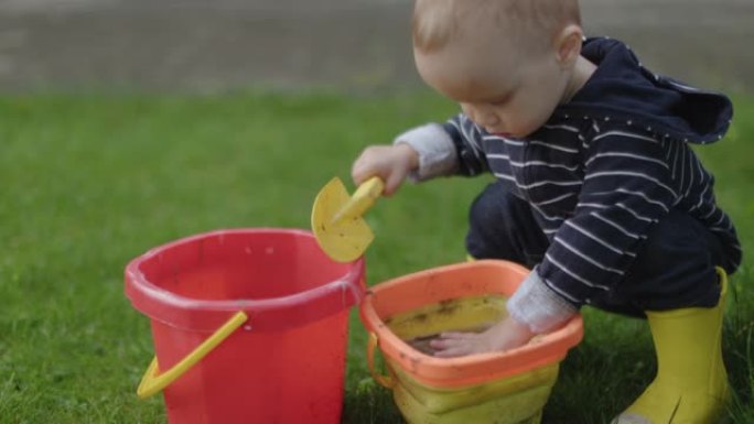 男婴蹒跚学步的孩子在户外用水桶玩泥沙和水