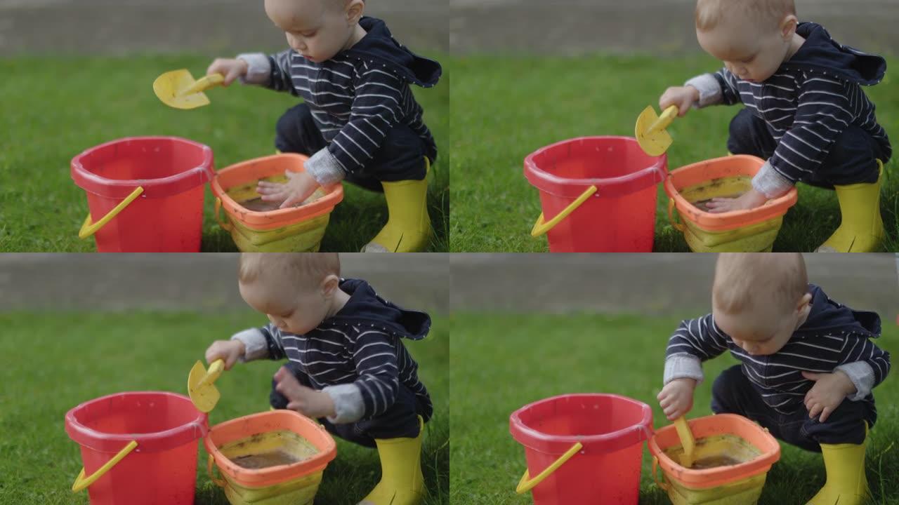 男婴蹒跚学步的孩子在户外用水桶玩泥沙和水