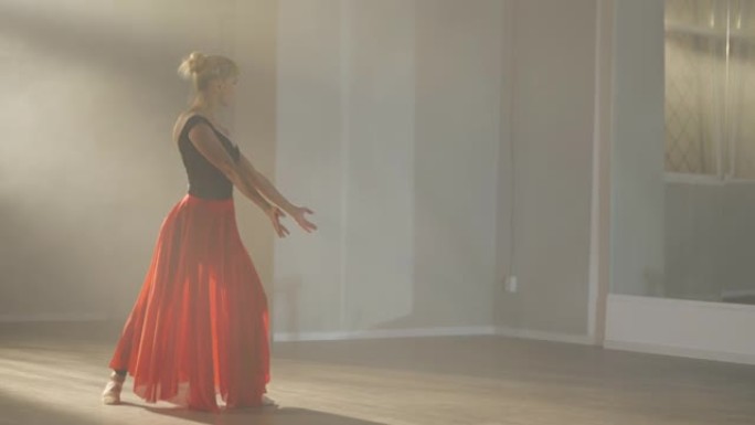 穿着猩红色裙子的勤奋苗条的职业芭蕾舞演员在慢动作舞蹈工作室排练表演。才华横溢的成人芭蕾舞演员在室内背