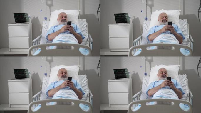 在医院病房使用手机的男性患者。老年男性患者在医院卧床休息时手持手机