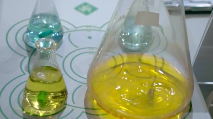 实验室电磁混合器在玻璃烧瓶中混合黄色溶液，用于医疗，化学，化妆品行业的产品。特写。运动中的镜头