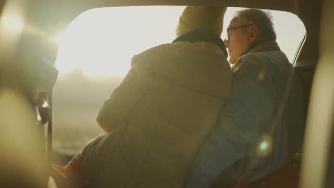 两个老年人在公路旅行中露营。坐在大型汽车后备箱里拥抱