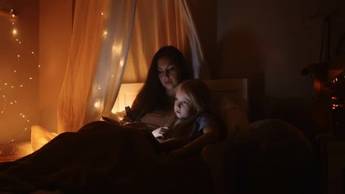 女人晚上为她的小孩读童话故事，妈妈抱着女儿看书