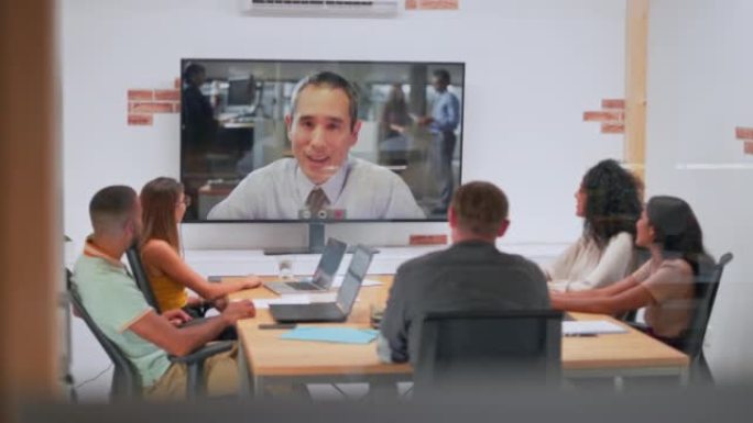 一个人在视频中与坐在会议室的人交谈
