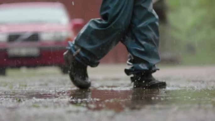 慢动作，一个穿着潮湿天气装备的孩子在大雨中行走