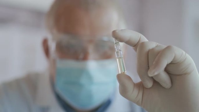 特写一位开发了冠状病毒疫苗的蒙面科学家拿着一瓶白色液体，并检查了疫苗。医生在用药前先看一下药