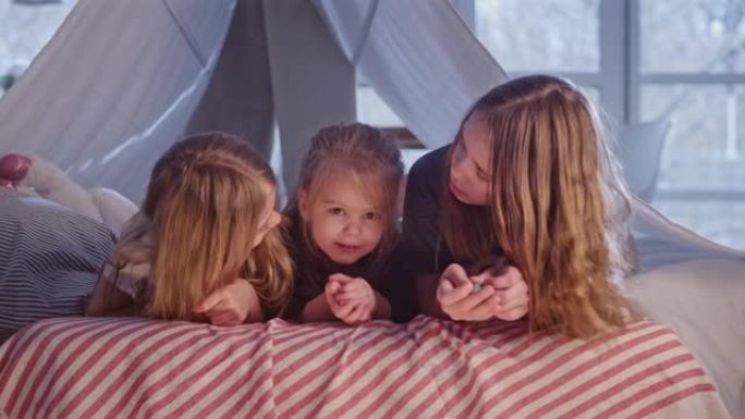 三个sistrers躺在舒适的天篷床上。看着相机，互相拥抱