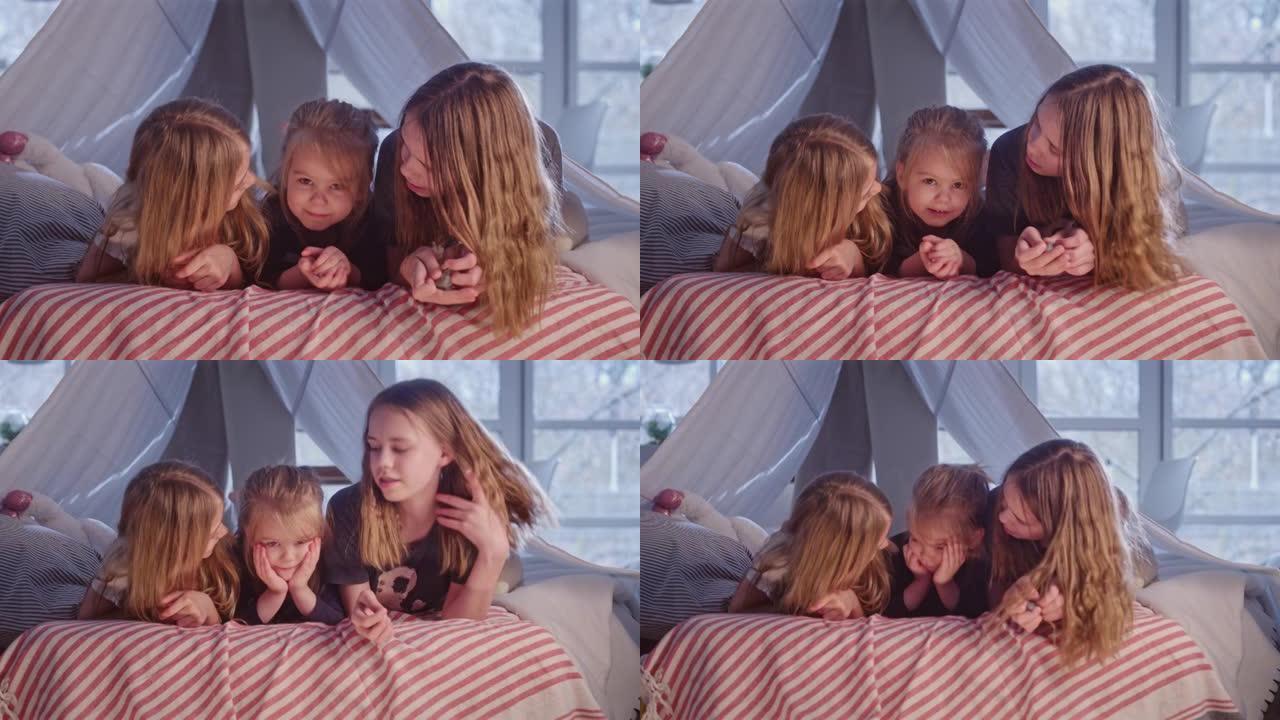三个sistrers躺在舒适的天篷床上。看着相机，互相拥抱