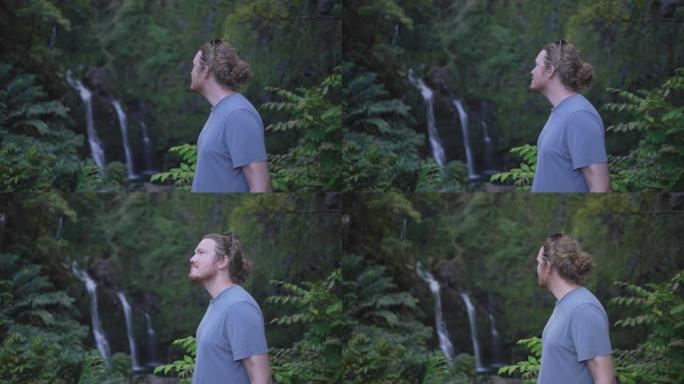 一个年轻人在森林里的特写镜头，瀑布在后面