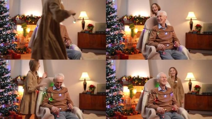 快乐的白人少女在圣诞花环上围着祖父跑来跑去。快乐无忧无虑的孙女在除夕夜在家和祖父母玩得开心。