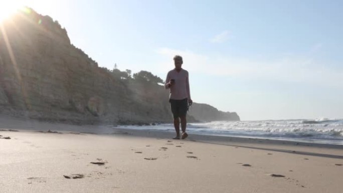 成熟的男人在日出时沿着空旷的海滩散步