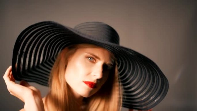 美丽诱人的金发女人用相机调情。戴着大而优雅的帽子和红色唇膏摆姿势