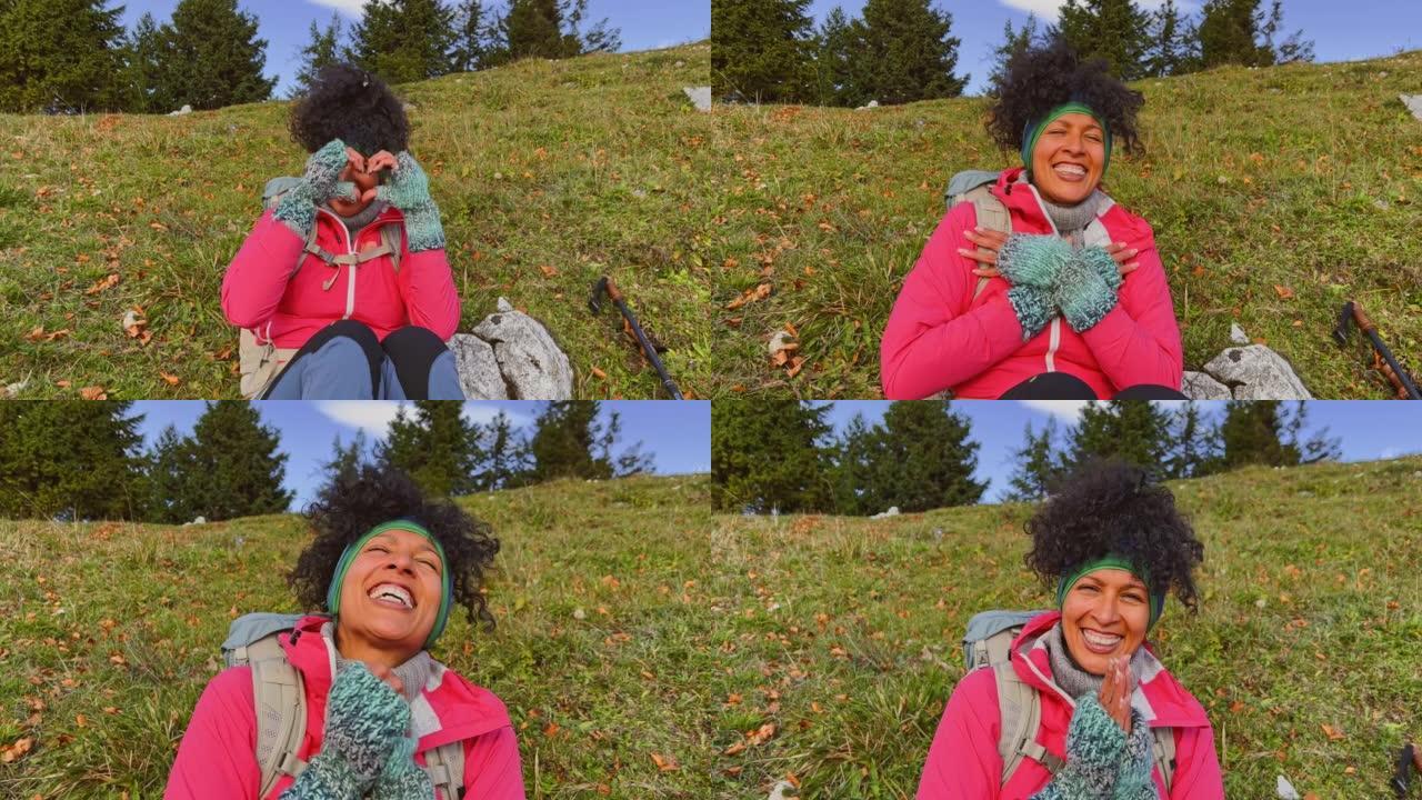 SLO MO女徒步旅行者坐在山顶上微笑着用手塑造一颗心