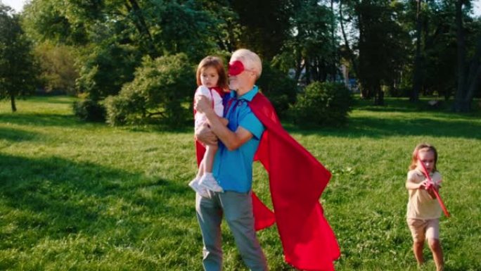 镜头前的特写镜头祖父和他的侄女穿着超级英雄套装和侄子在公园中央的飞机上玩耍时