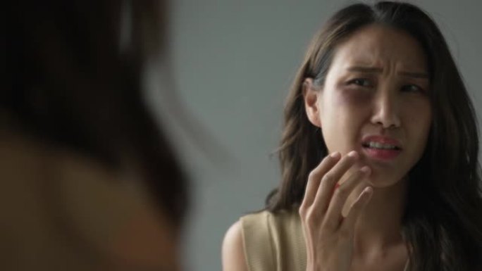 一个害怕的年轻亚洲女人看着镜子里的自己脸上有淤青。家庭暴力中女人被男人暴打。家庭问题，家庭暴力。