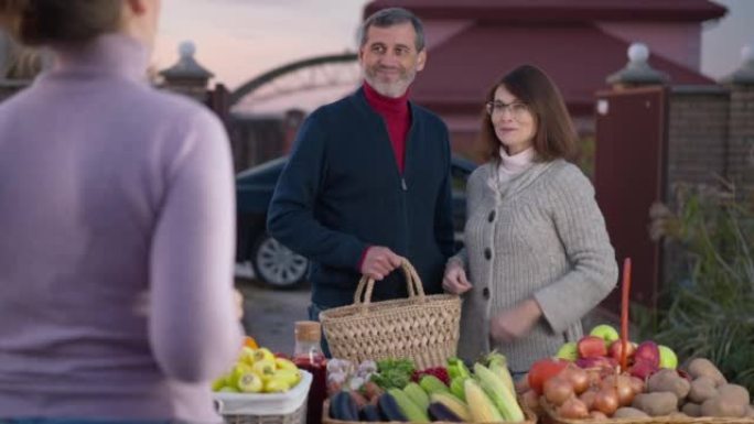 快乐满意的买家在农场市场上向卖家传递现金，感谢步行到汽车上。晚上在户外出售有机水果和蔬菜的模糊女人的