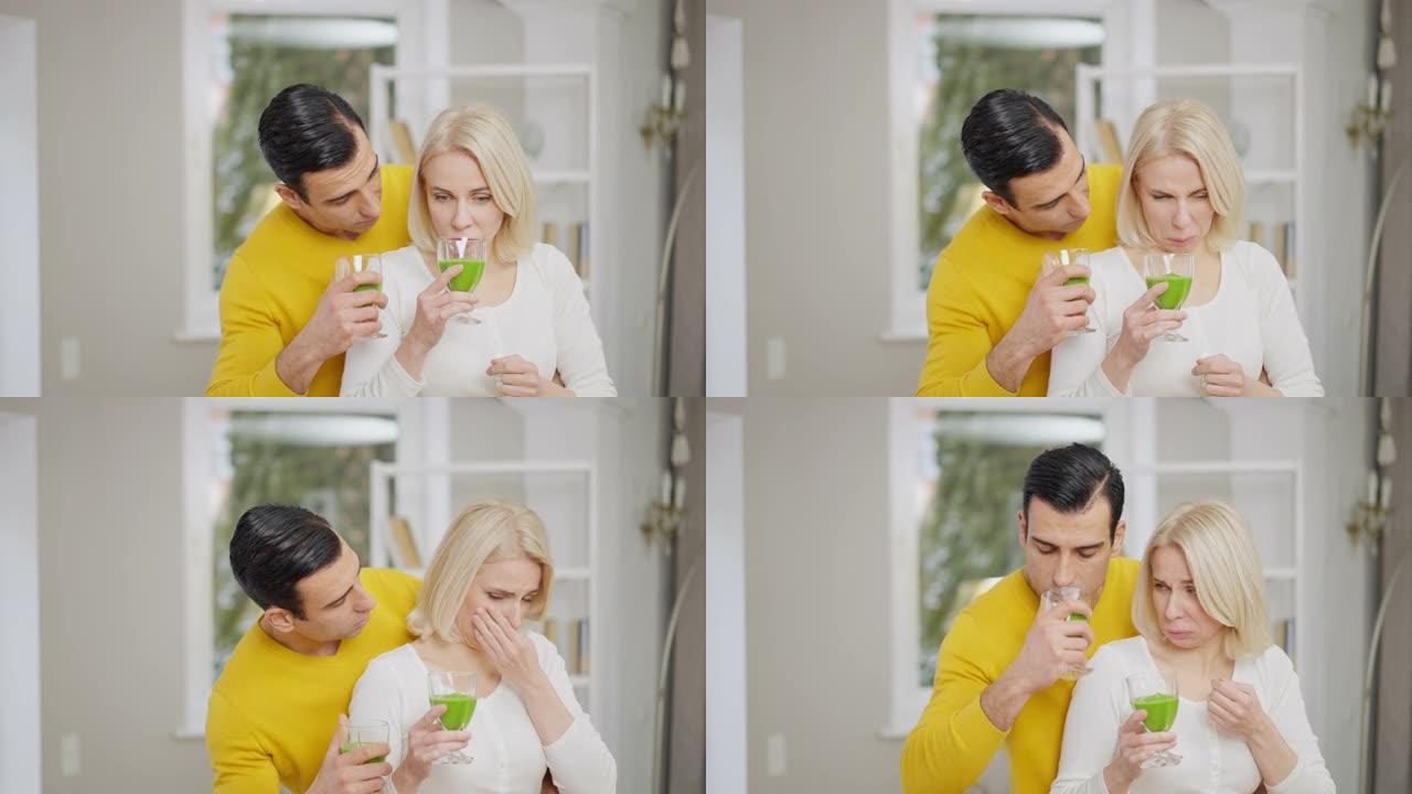 年轻夫妇的肖像闻到健康的绿色冰沙，令人厌恶的面部表情。美丽的高加索女人和英俊的中东男人在家喝健康饮料