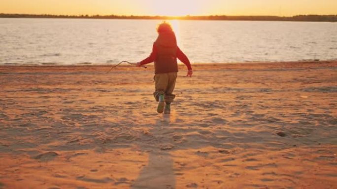 快乐的小男孩在日落，童年的时刻和幸福中奔跑在河的沙滩上