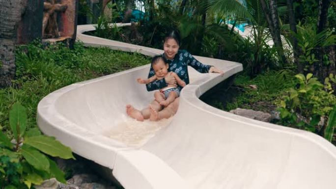 快乐的母亲和她的男婴在水上公园滑梯上
