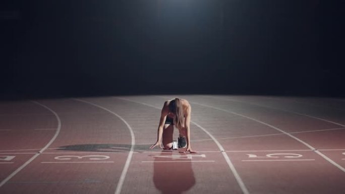 体育场内一名黑暗中的妇女正准备在赛道上开始比赛。慢动作女在黑暗中从体育场绝食开始