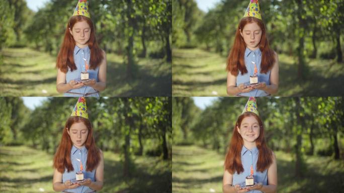 可爱的高加索红发少女在公园生日时吹蛋糕蜡烛的肖像微笑着看着相机。快乐美丽的少年在春夏公园摆姿势度假野