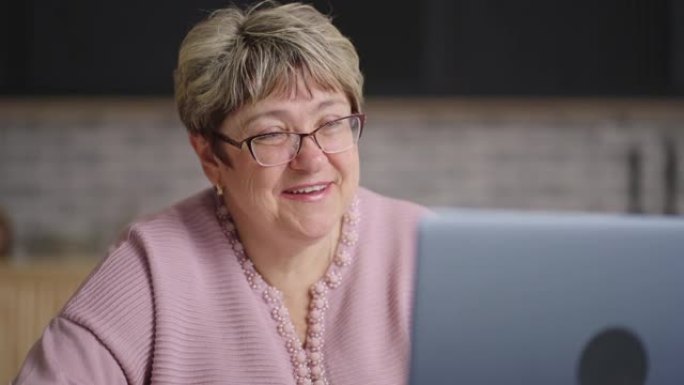 快乐的祖母在笔记本电脑上通过视频聊天与家人聊天，退休女士周末坐在家里的厨房里