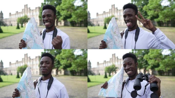 快乐的非裔美国游客在户外的欧洲小镇用纸质地图和双筒望远镜摆姿势。快乐兴奋的英俊年轻人看着相机微笑示意