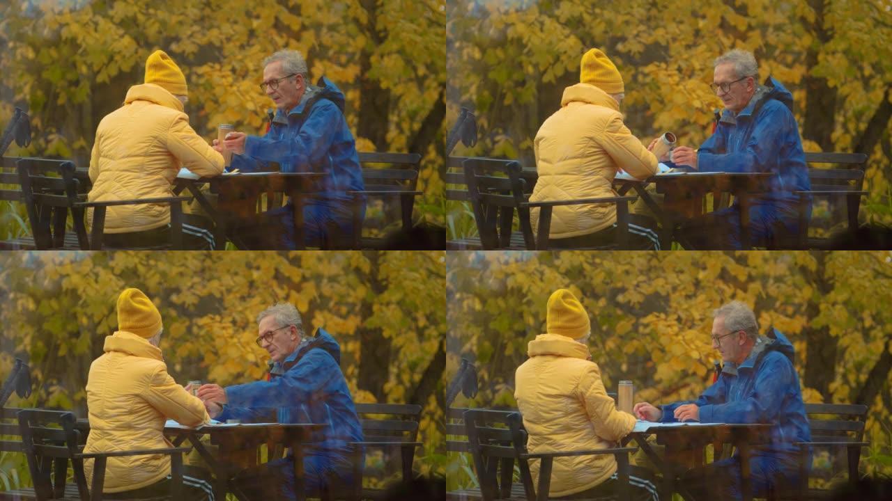 北欧老年夫妇散步休息，在公园餐桌上喝茶。从室内观看