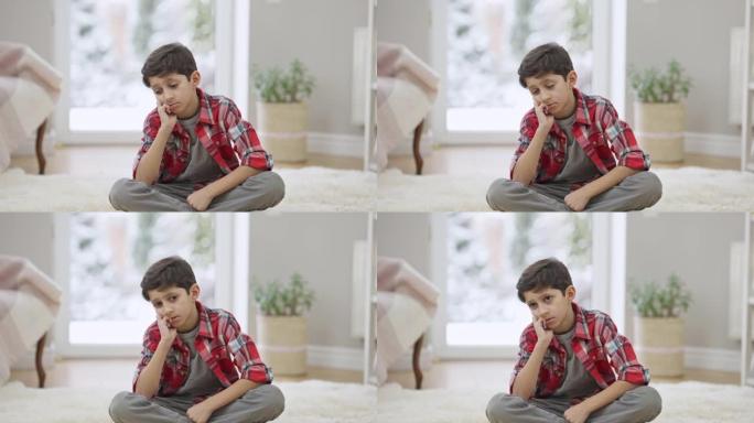 悲伤沮丧的中东男孩坐在家里的地毯上思考。孤独沮丧被欺负的孩子独自在室内的肖像。童年问题和抑郁概念。