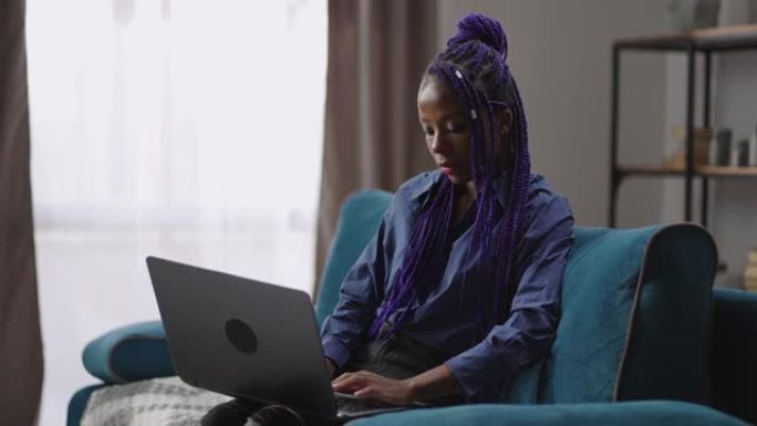 成年黑人妇女周末在家使用笔记本电脑，坐在客厅的沙发上上网，在社交网络中聊天