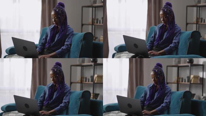 成年黑人妇女周末在家使用笔记本电脑，坐在客厅的沙发上上网，在社交网络中聊天
