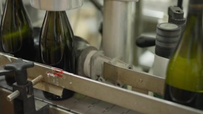 葡萄酒厂的近距离自动开瓶机，玻璃瓶通过。酒厂室内饮料包装和标签的过程。工业概念。