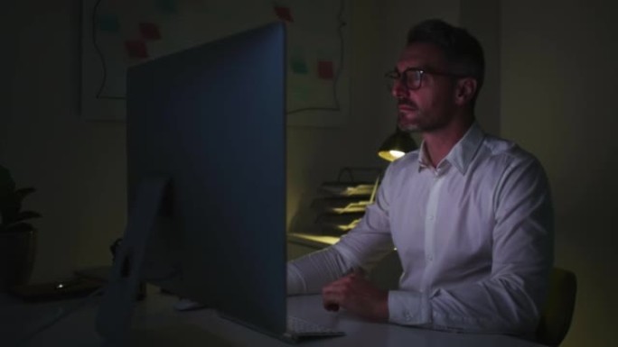 疲惫的商人深夜在电脑上工作时按摩酸痛的肩膀。公司在办公室加班时坐得太久感到压力