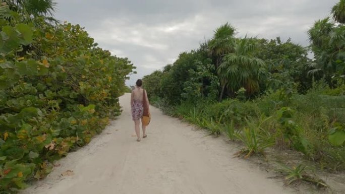 女人沿着丛林小路走向海滩