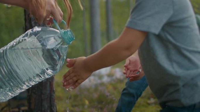 女人正在从小男孩的手上倒水，孩子正在森林营地洗手