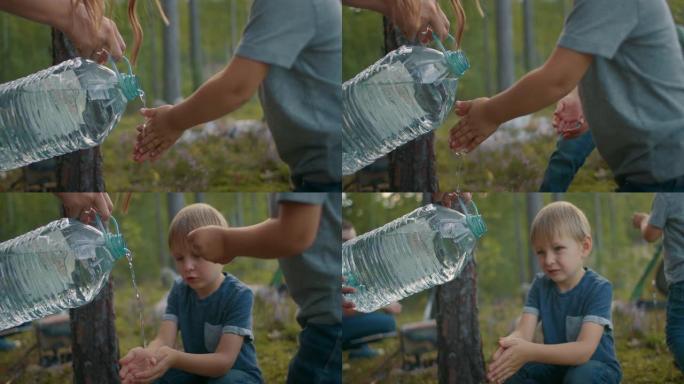 女人正在从小男孩的手上倒水，孩子正在森林营地洗手