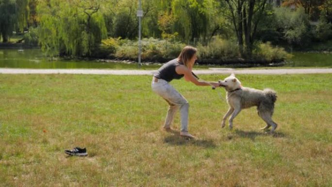年轻女子带着她的白色大皮毛脏狗，因为城市公园湖里的绿色脏水