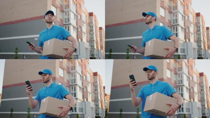 戴眼镜的邮递员携带包裹，并通过手机查看收货地址。搜索送货客户的地址。带帽和盒子的送货员