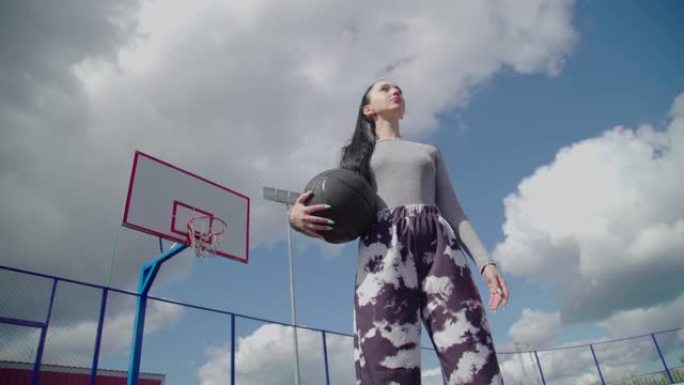 迷人的黑发女孩拿着黑色篮球向一边看。