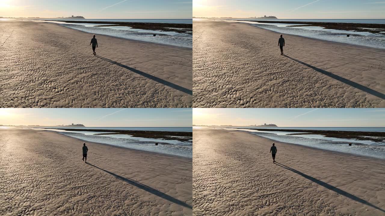 男子在空旷的海滩上漫步的鸟瞰图